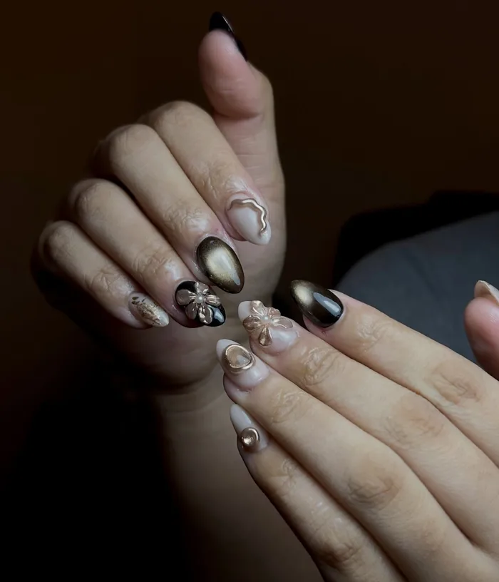 A gold chrome set with raised 3D flowers and a dark marbled accent nail